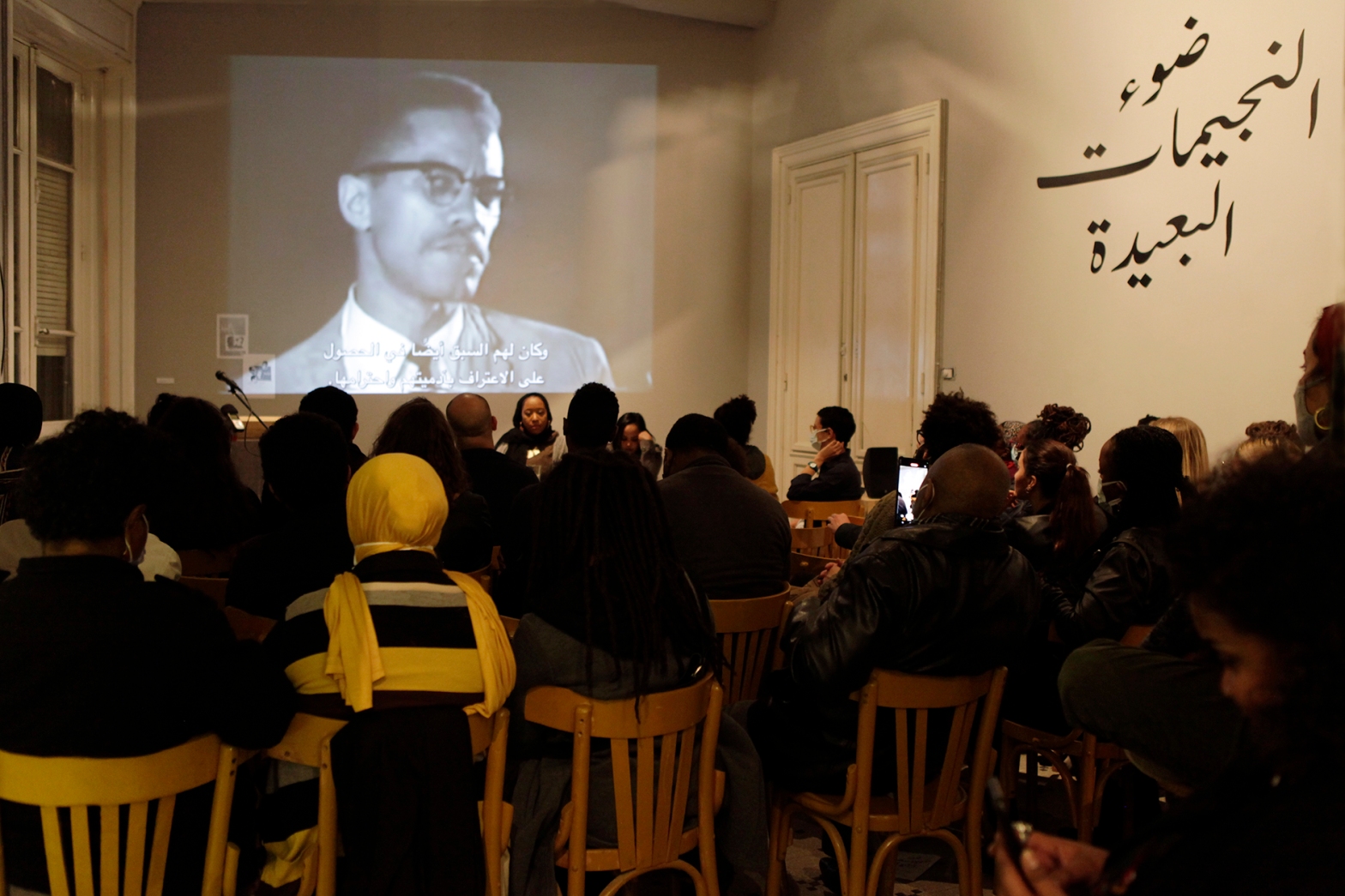 Projection of Malcom X on wall, artist Nsenga Knight and Translator Samah Gafar in from of audience of Cairenes at the COntemporary Image Collective in Cairo Egypt. Nsenga Knight performs her X Speaks performance art and social practice work